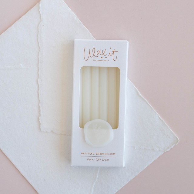 Caixa branca com seis varetas de cera brancas para lacre sobre papel branco e fundo rosa claro