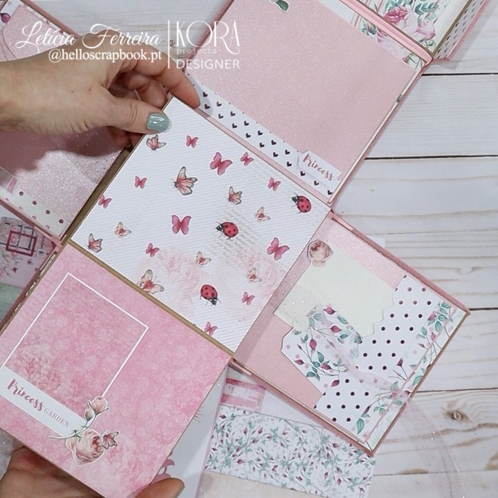 Livro artesanal rosa com padrões de borboletas, joaninhas e flores sobre fundo de madeira branca