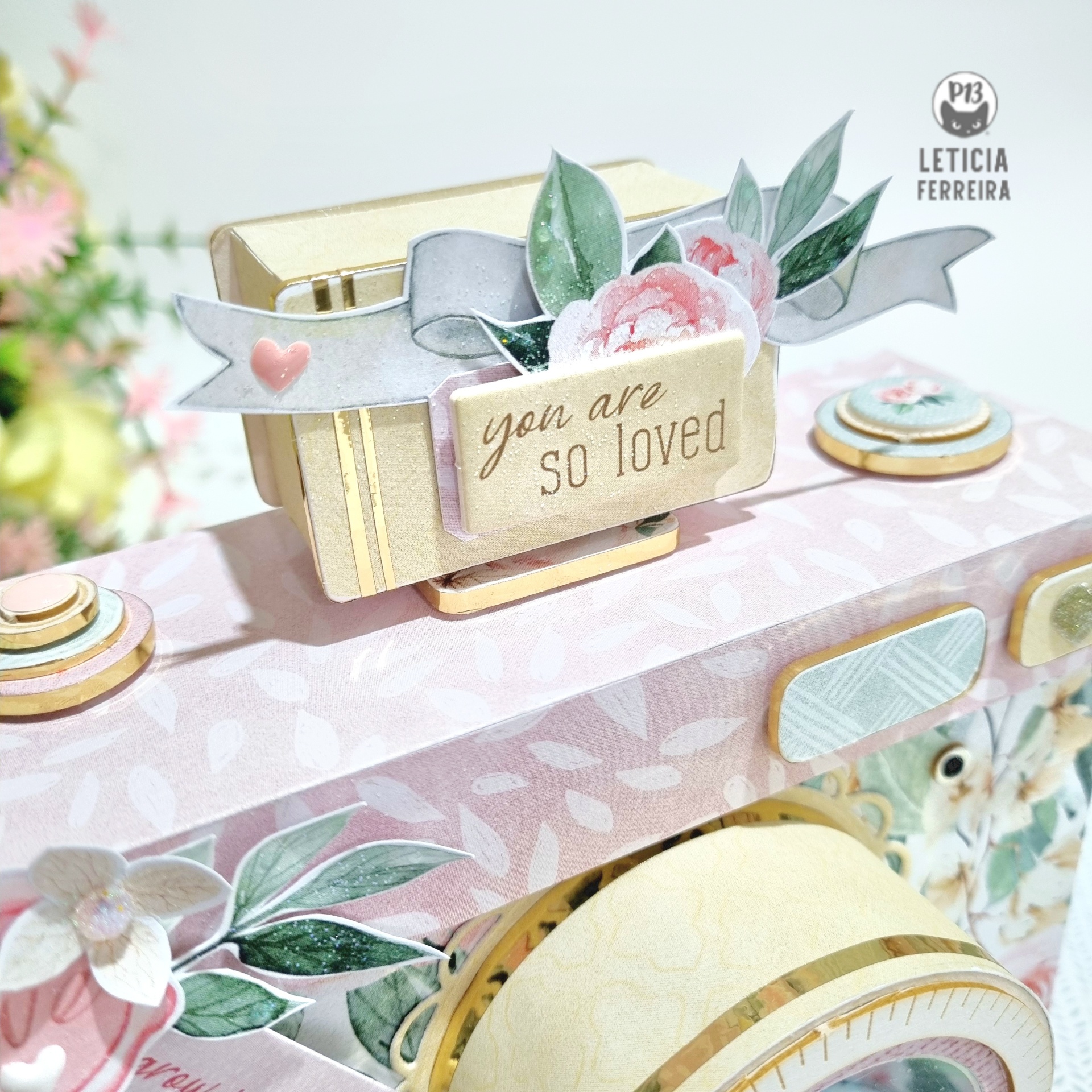 Máquina de costura decorativa rosa com detalhes dourados e flores, etiqueta com texto em inglês