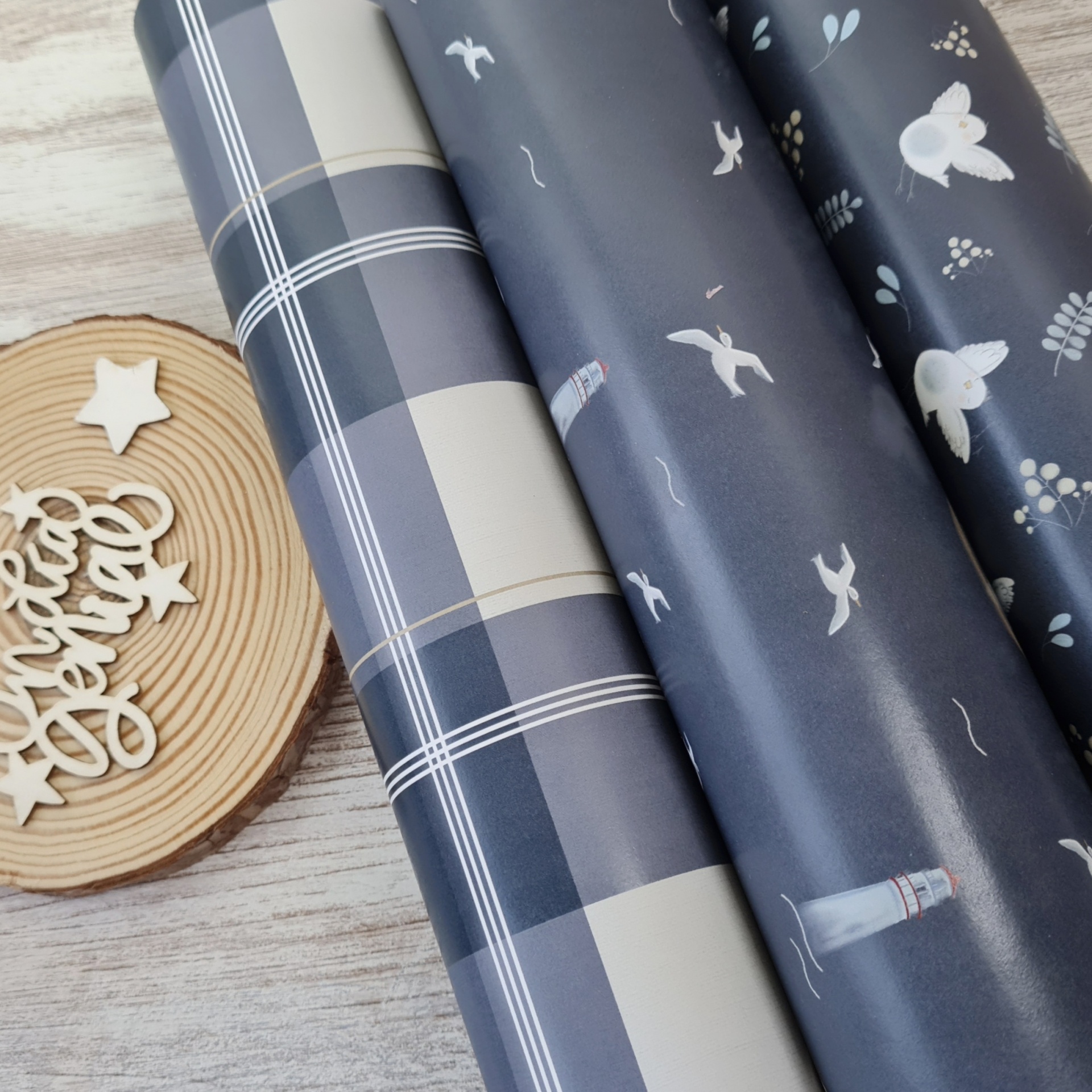 Três rolos de papel de embrulho azul e cinzento com padrões variados junto a base redonda de madeira com elementos decorativos