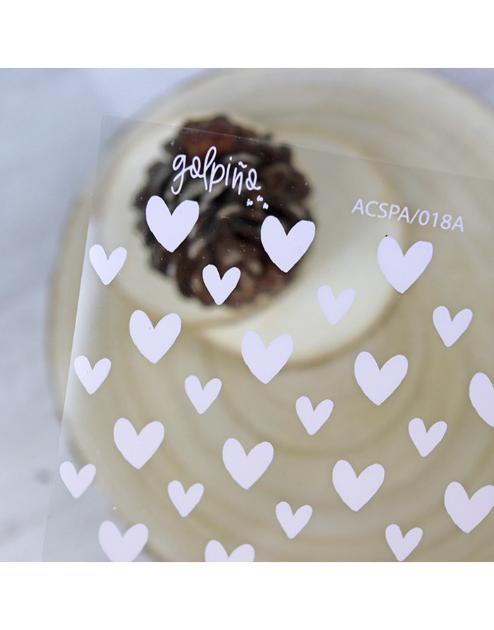 Bolo branco decorado com creme em espiral e enfeite castanho, embalado em plástico com corações brancos e texto impresso.