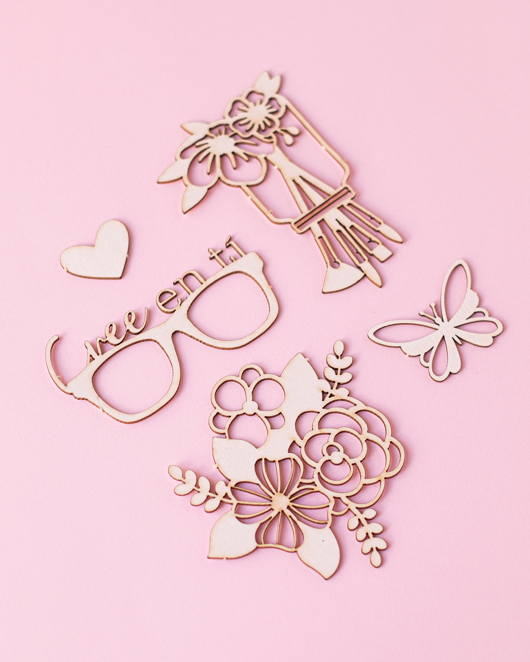 Recortes decorativos em madeira clara sobre fundo rosa