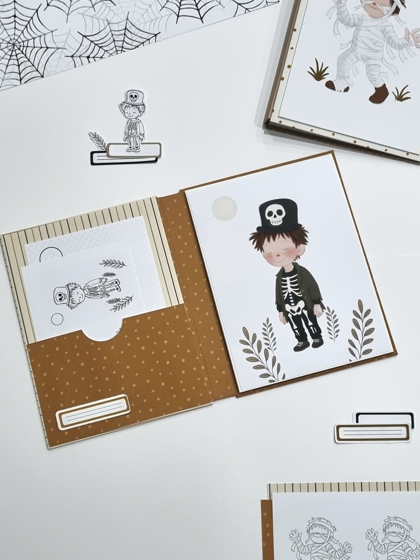Papelaria de Halloween com pretos e castanhos, ilustrações de esqueletos em papel e recortes