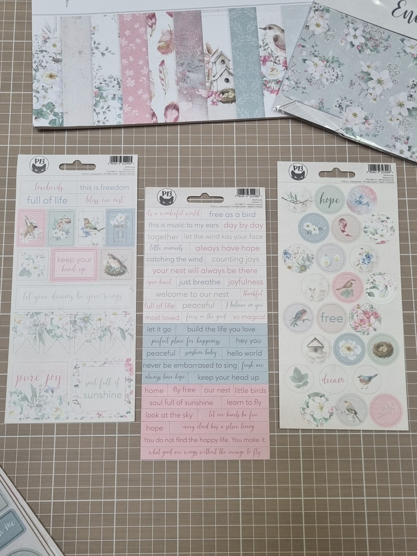 Papéis decorativos e autocolantes de scrapbooking com padrões florais e pássaros em tons pastel.