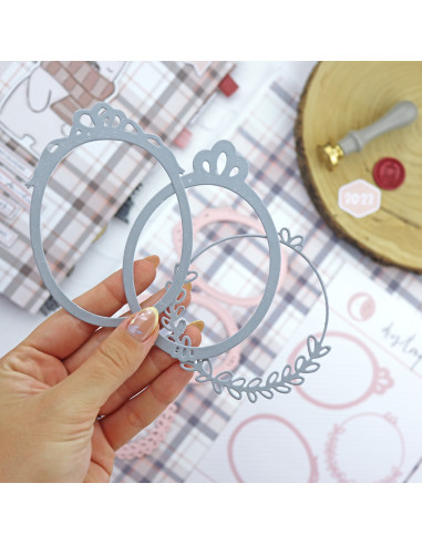 Molduras metálicas cinza decorativas seguradas à mão sobre mesa com padrões e carimbos