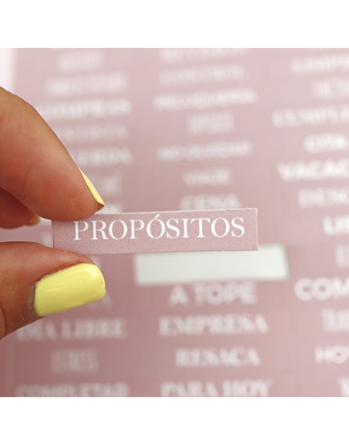 Etiqueta transparente com a palavra 'PROPÓSITOS' segurada por mão com unhas amarelas