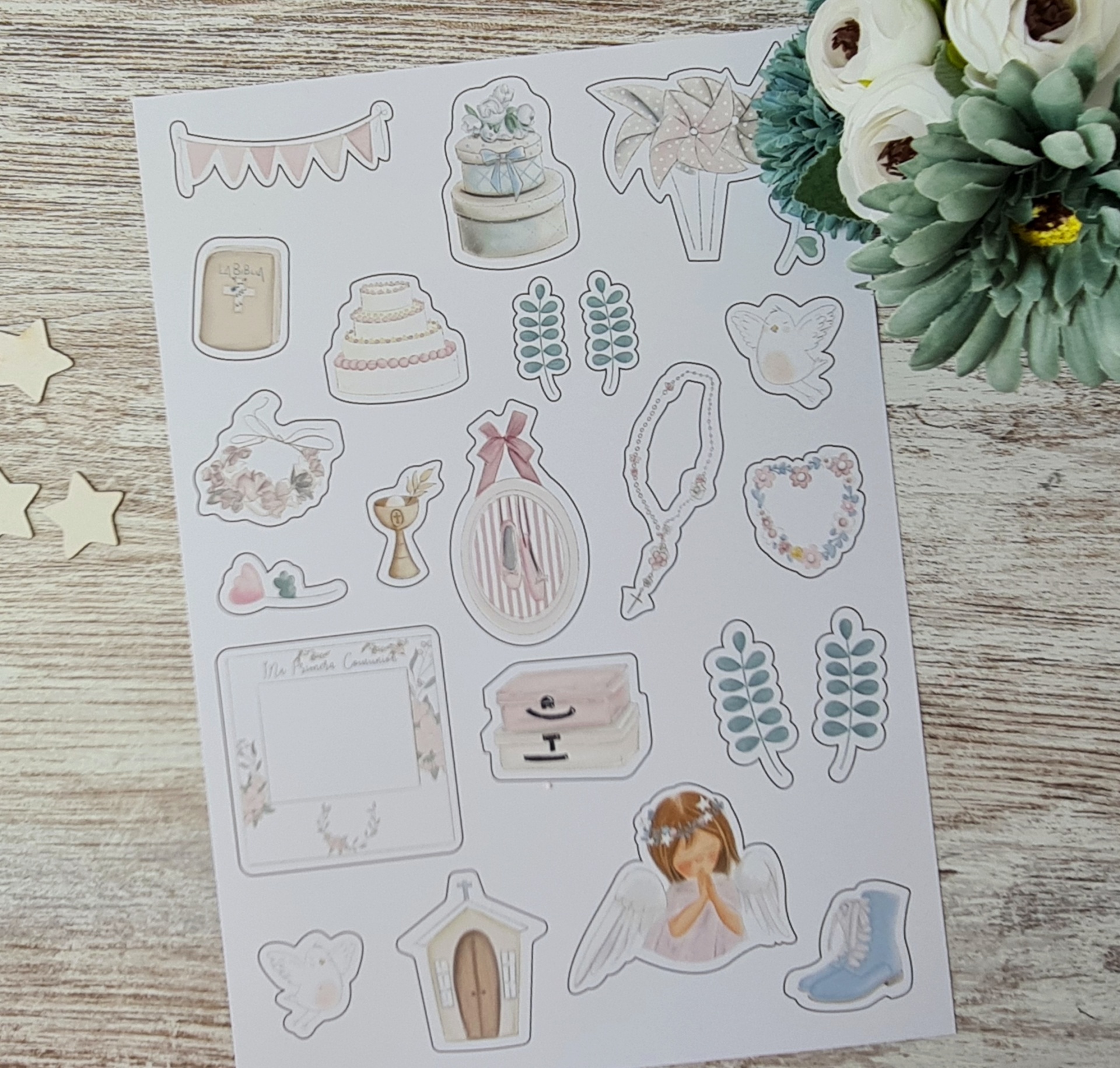 Folha de autocolantes decorativos variados sobre mesa de madeira clara com arranjo floral ao lado.