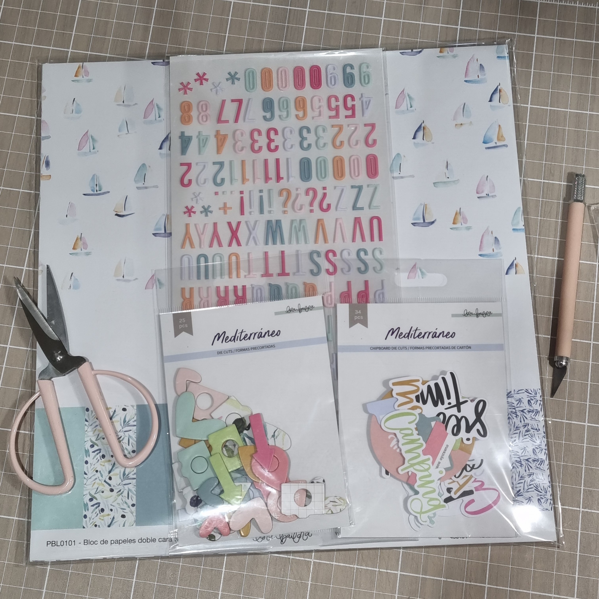 Conjunto de papelaria para scrapbooking com veleiros, autocolantes de letras e números, recortes coloridos, tesoura rosa e ferramenta de corte.