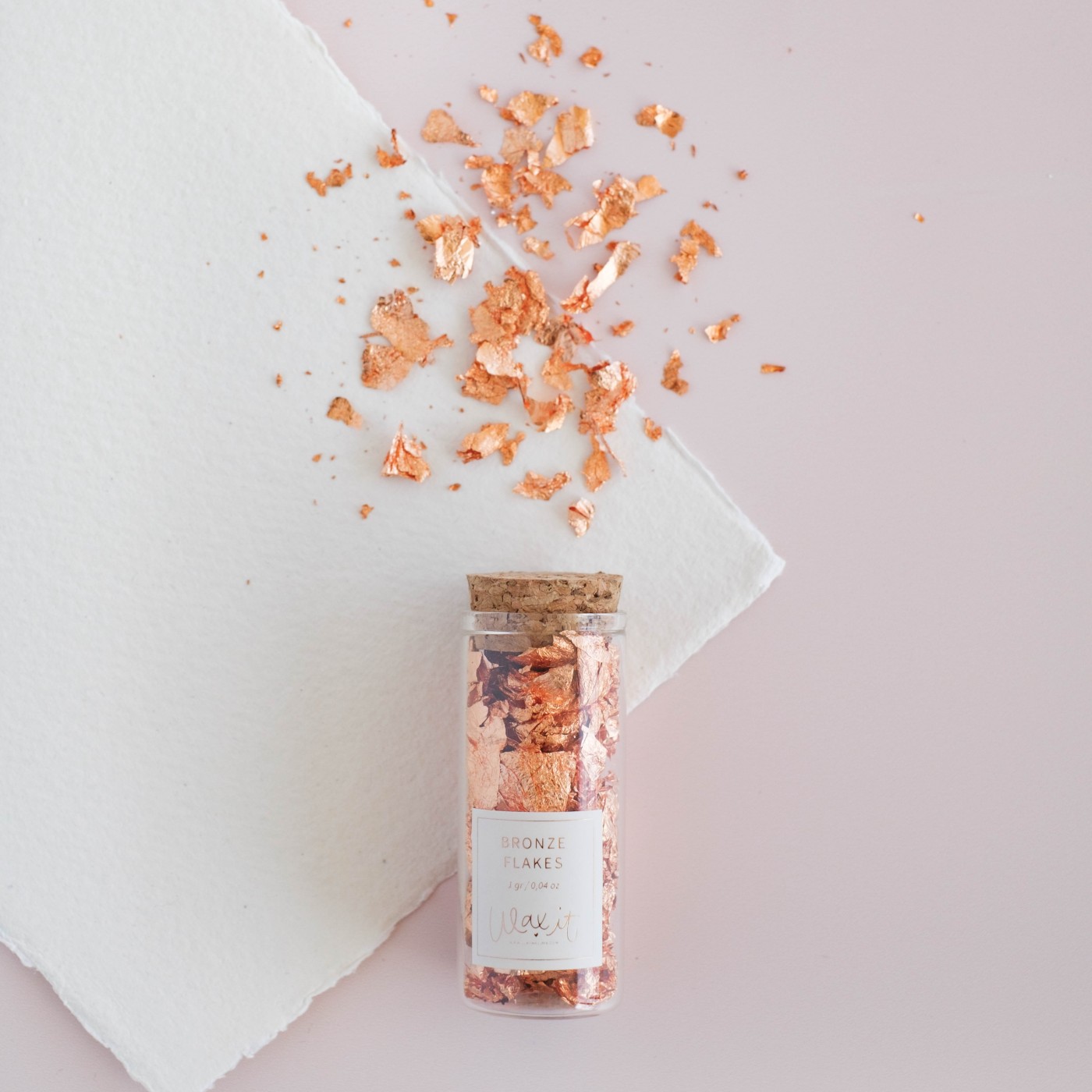 Frasco com flocos cor de cobre numa superfície branca sobre fundo rosa claro