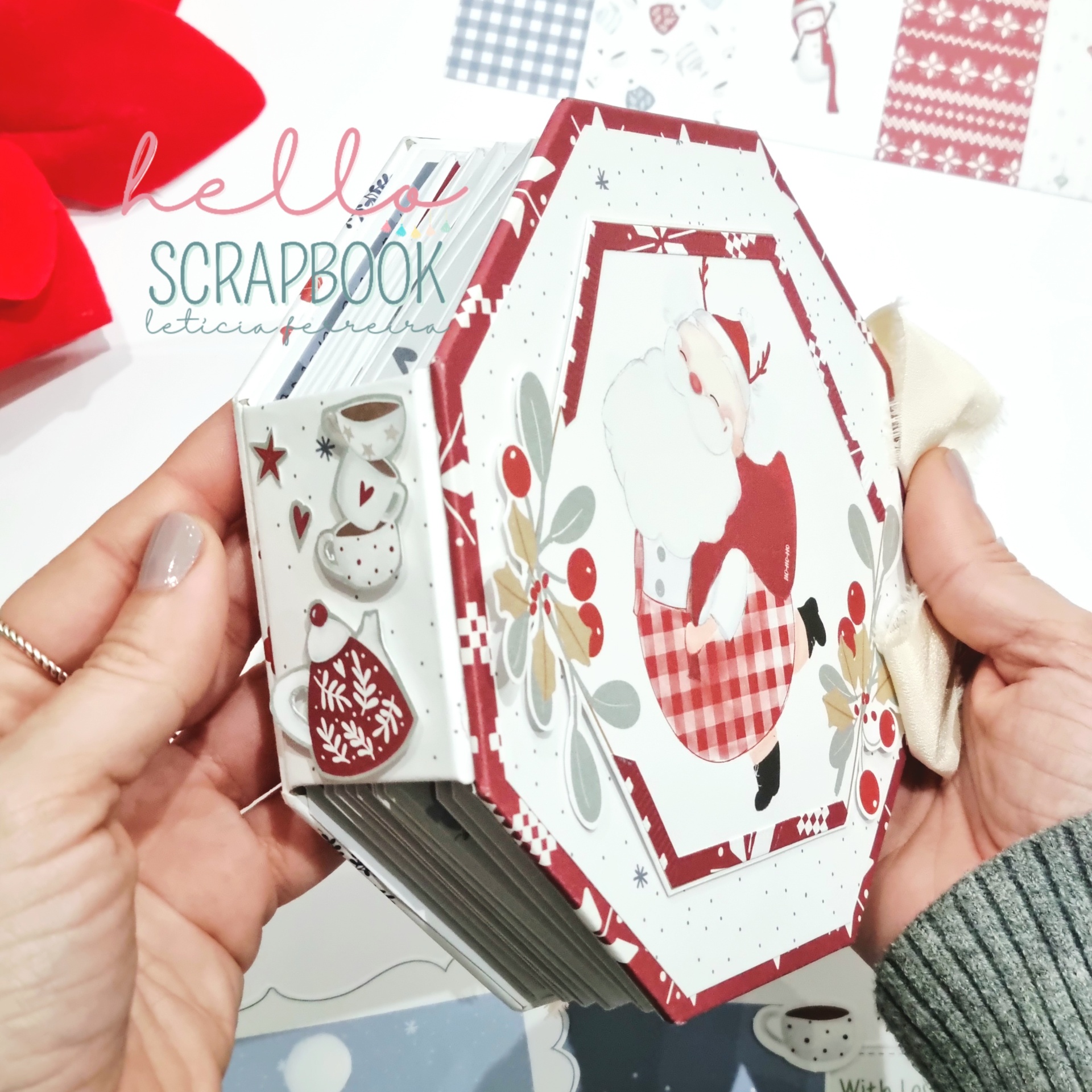 Álbum de scrapbook octogonal com decoração natalícia a cores e mão segurando.