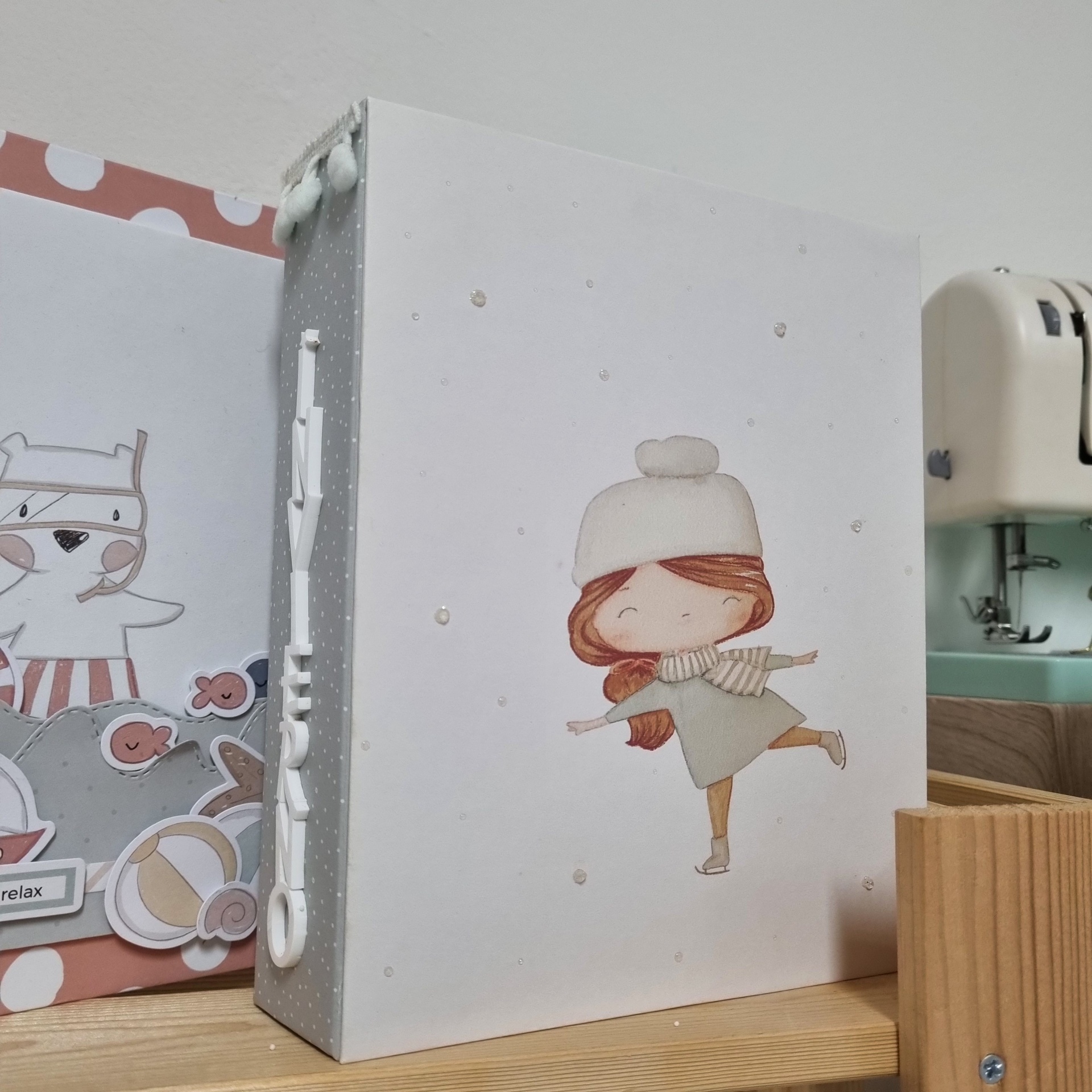 Álbum para fotografias artesanal em com ilustração de menina a patinar e palavra Inverno na lateral.