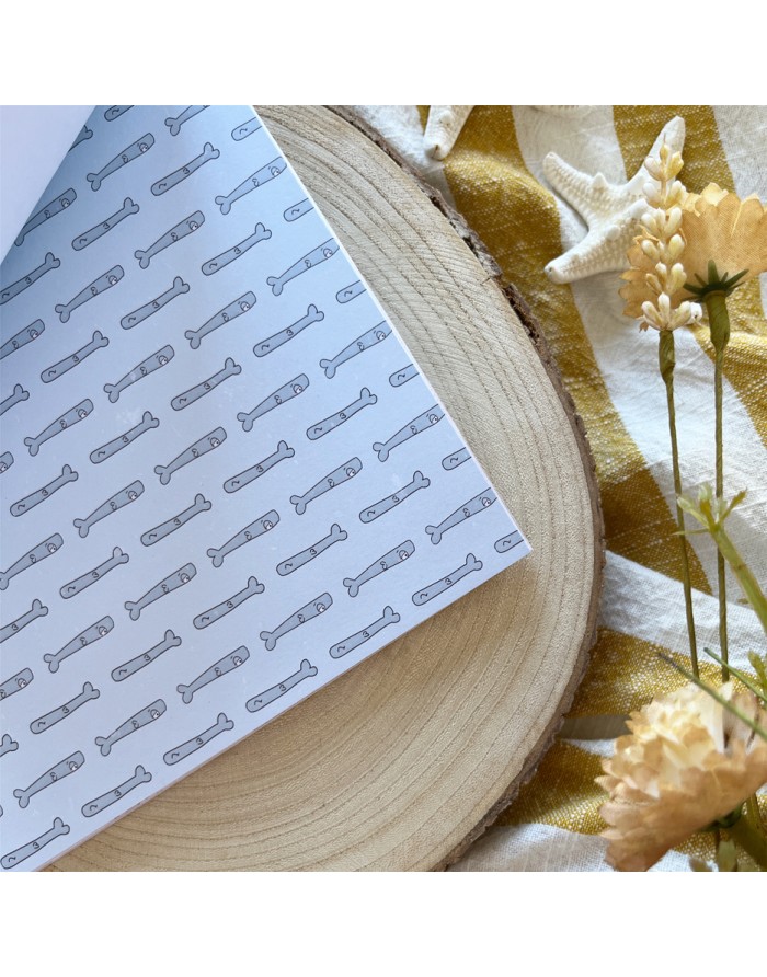 Livro com capa branca e padrão de facas cinzentas sobre madeira e tecido amarelo com flores e estrela do mar.