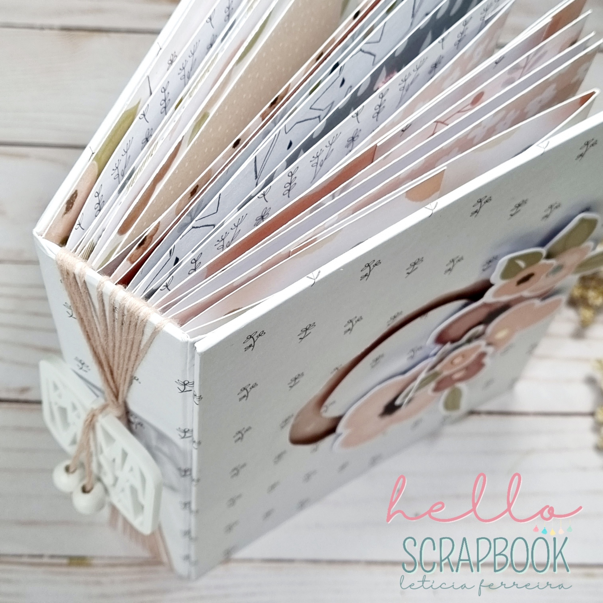 Álbum scrapbook branco decorado com flores e laços, aberto sobre superfície de madeira clara