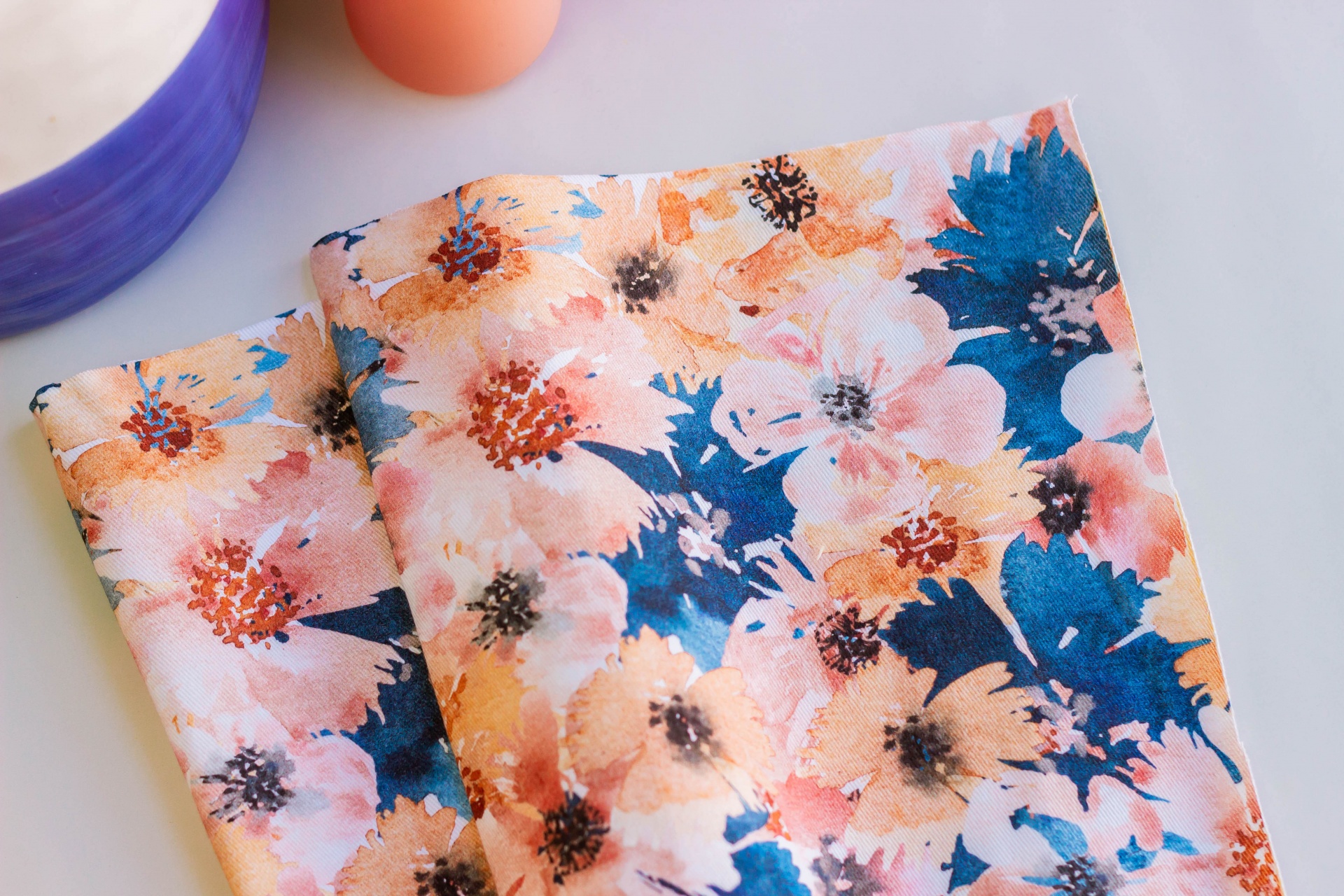tecido com padrão floral colorido, tigela roxa e ovo laranja