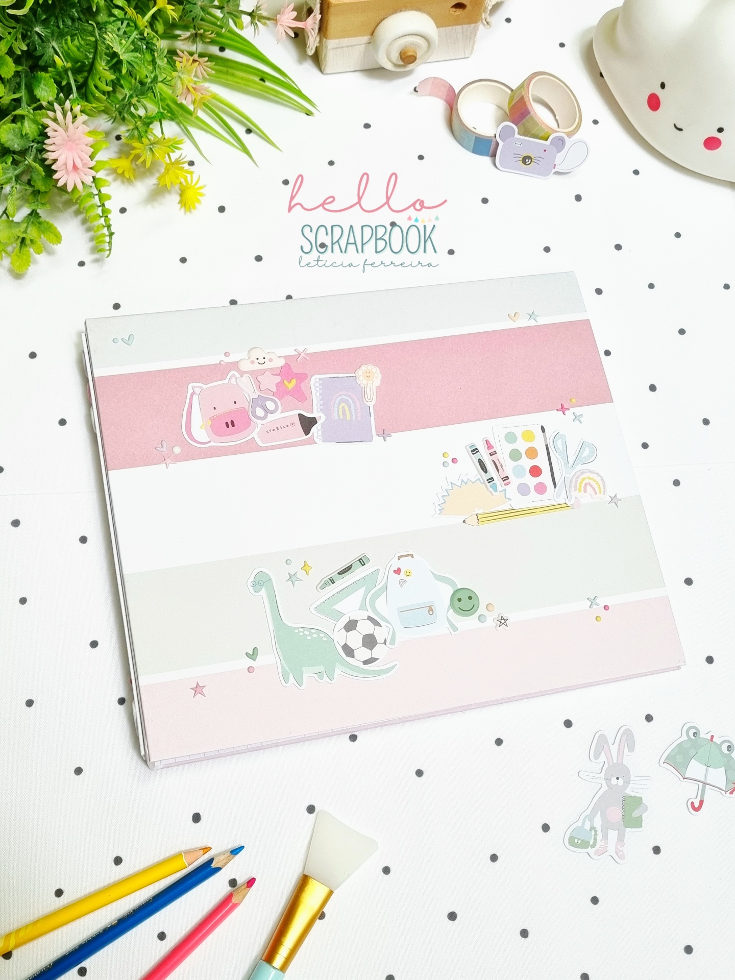 Caderno de scrapbook colorido com ilustrações infantis sobre superfície branca com pontos pretos e materiais de arte