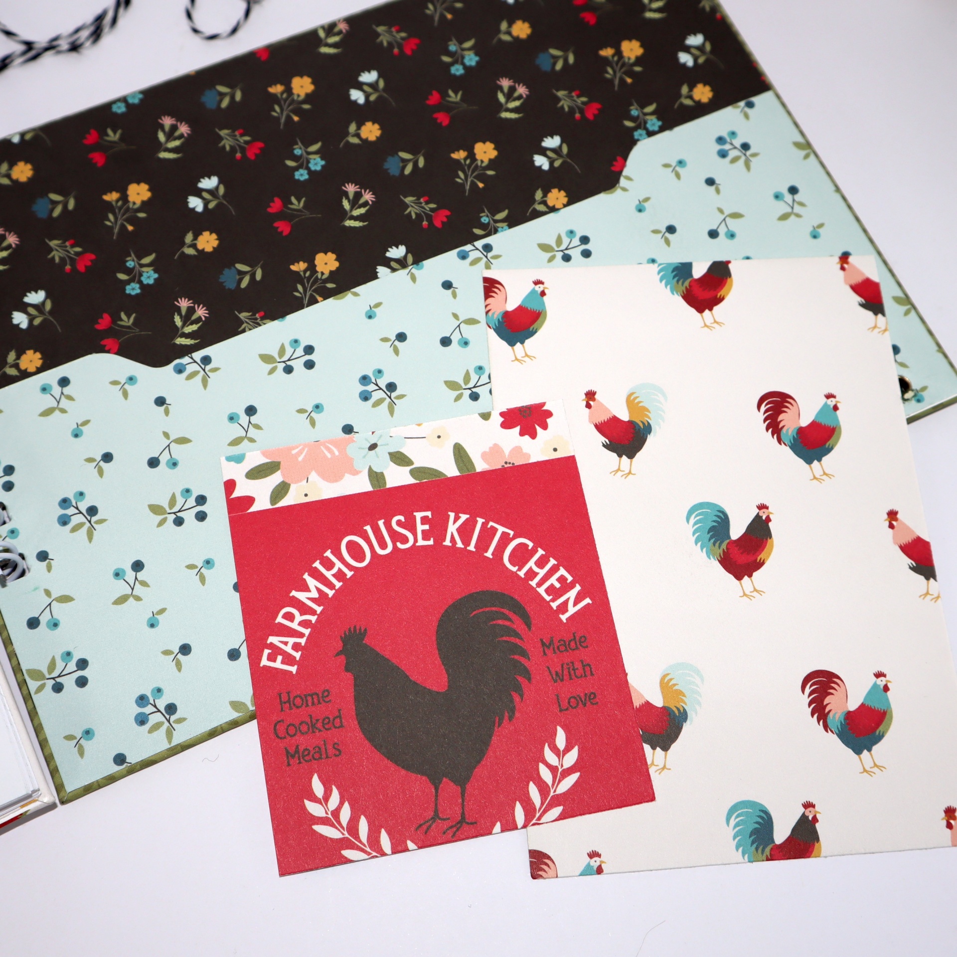 Papelaria com padrões de galos, flores e cartão vermelho com texto e galo preto.