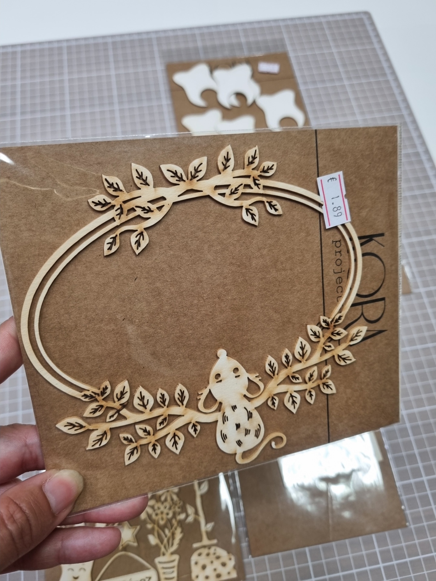 Enfeite de madeira com ramos, folhas e rato em papel castanho com etiqueta de preço €1,89