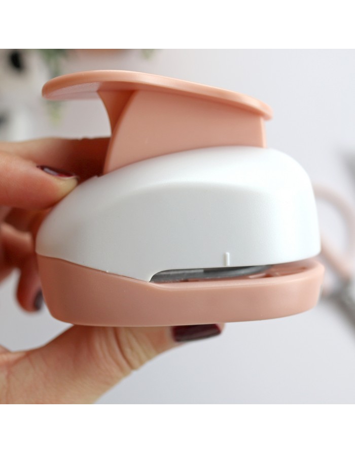 Ferramenta para cortar ou fechar papel branca e rosa salmão segurada por mão