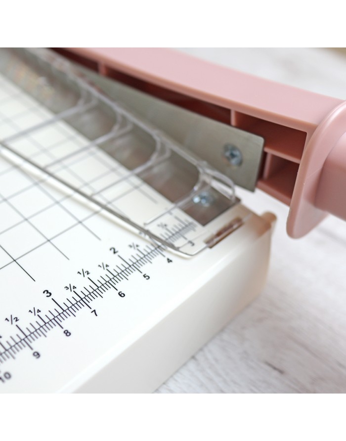 Guillotina de papel branca e rosa com régua graduada em centímetros e polegadas.