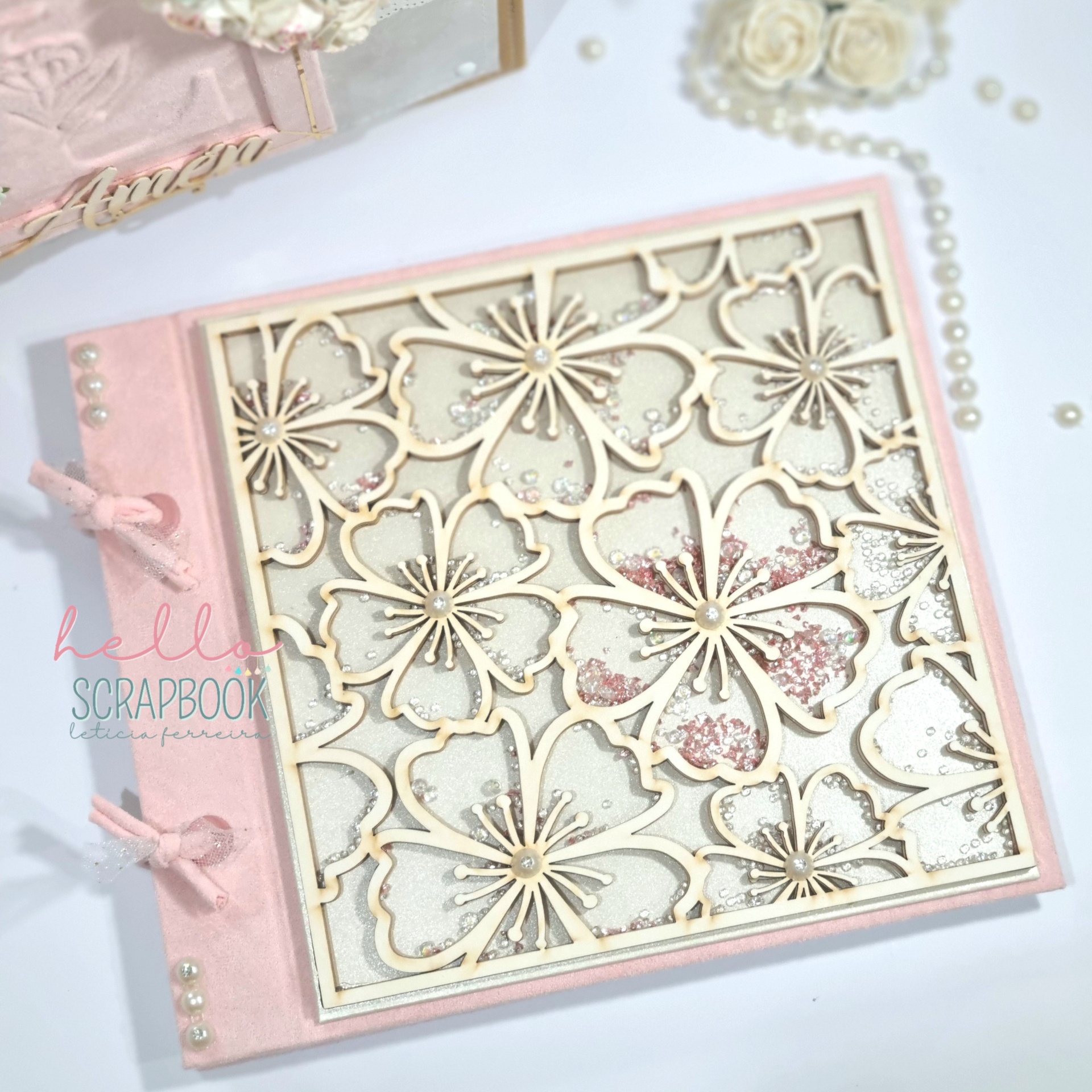 Livro de scrapbook com capa rosa clara e gravação floral em madeira clara, decorado com pérolas e laços de fita rosa