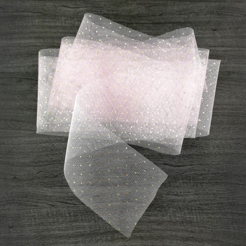 Tecido de tule branco com pontos dourados sobre madeira escura