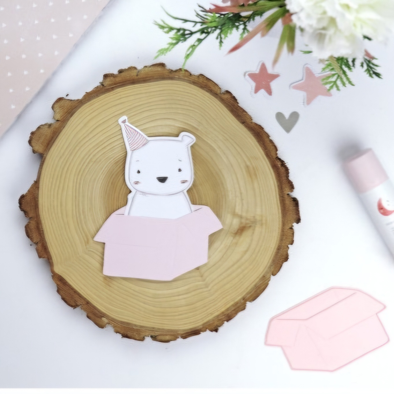 Cartão decorativo com urso em caixa sobre base de madeira rodeado por decoração