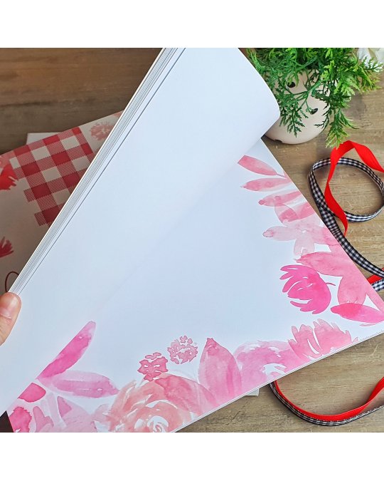 Bloco de folhas decoradas com flores cor de rosa em mesa de madeira com fitas e planta