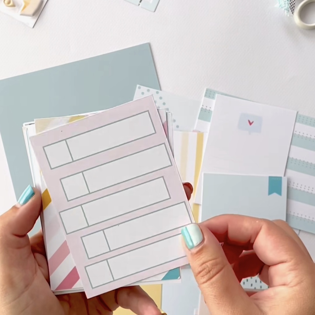 Mãos seguram blocos de notas coloridos com diferentes padrões e uma letra V visível.