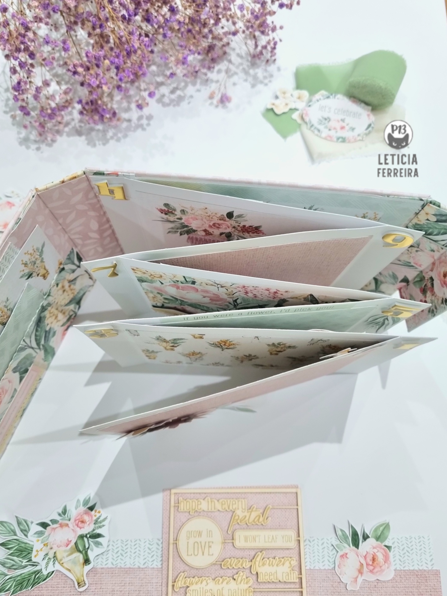Álbum artesanal floral aberto com várias páginas, flores secas lilás e etiqueta verde com texto 'P13 LETICIA FERREIRA'.