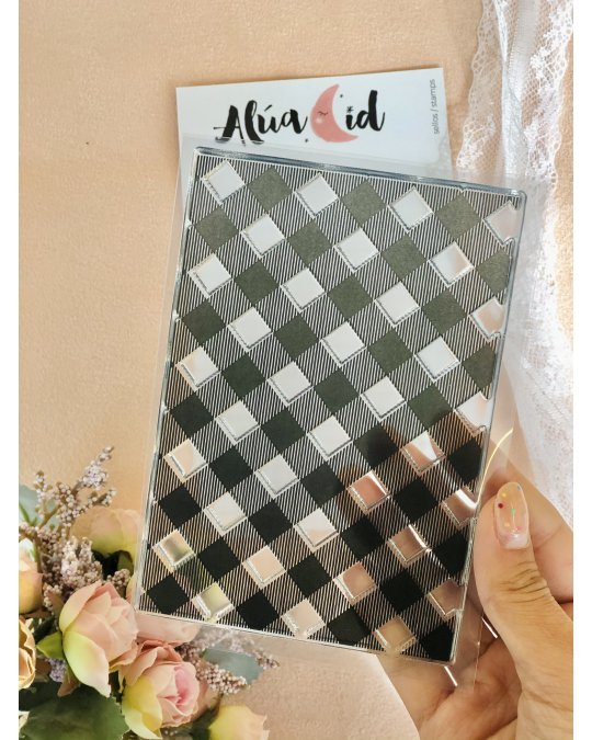 Caderno com capa xadrez preto e branco em plástico transparente, etiqueta Alúa Cid, flores ao lado