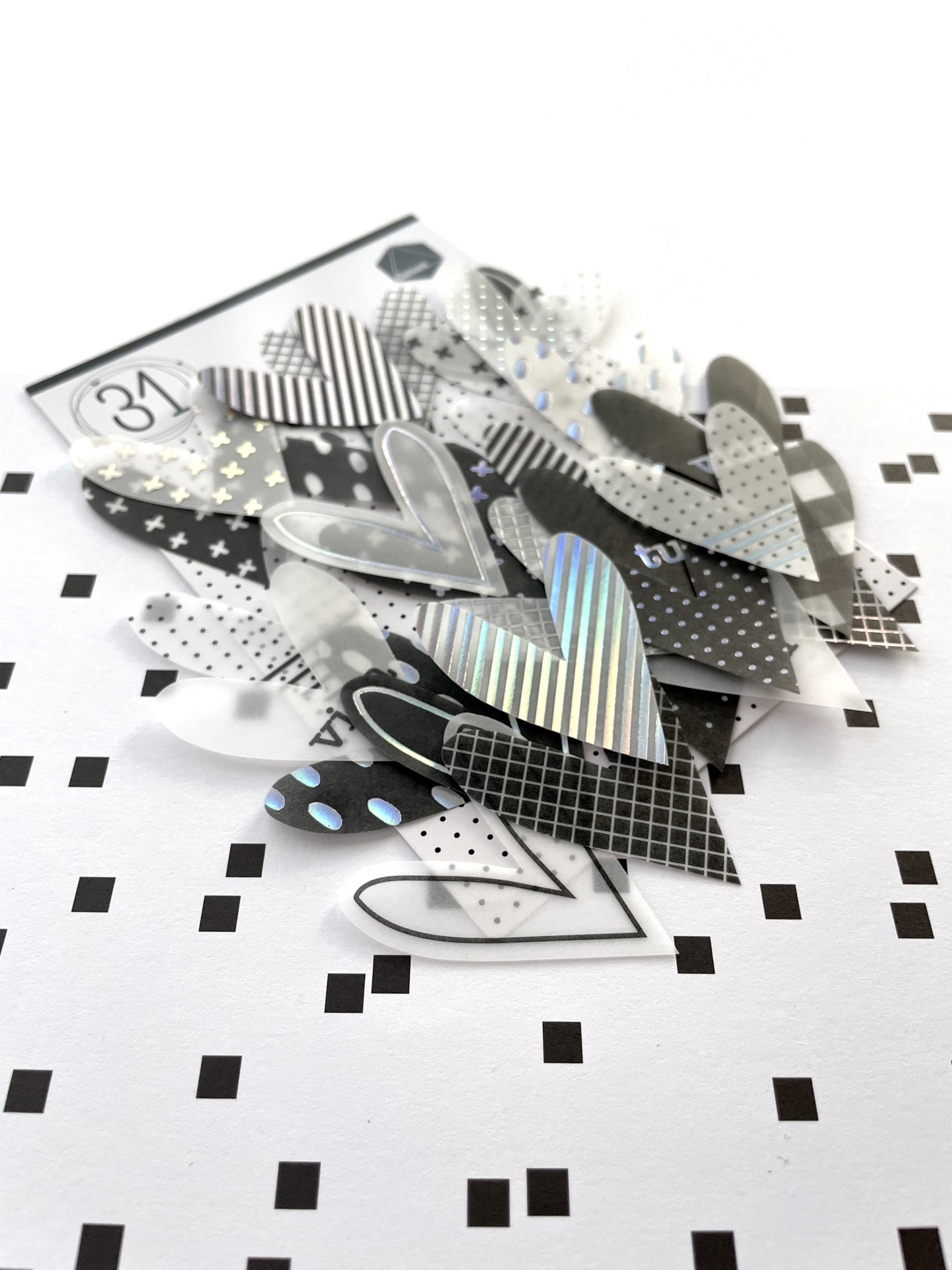 Vários corações decorativos em preto, branco e prateado com padrões variados sobre fundo branco com quadrados pretos.