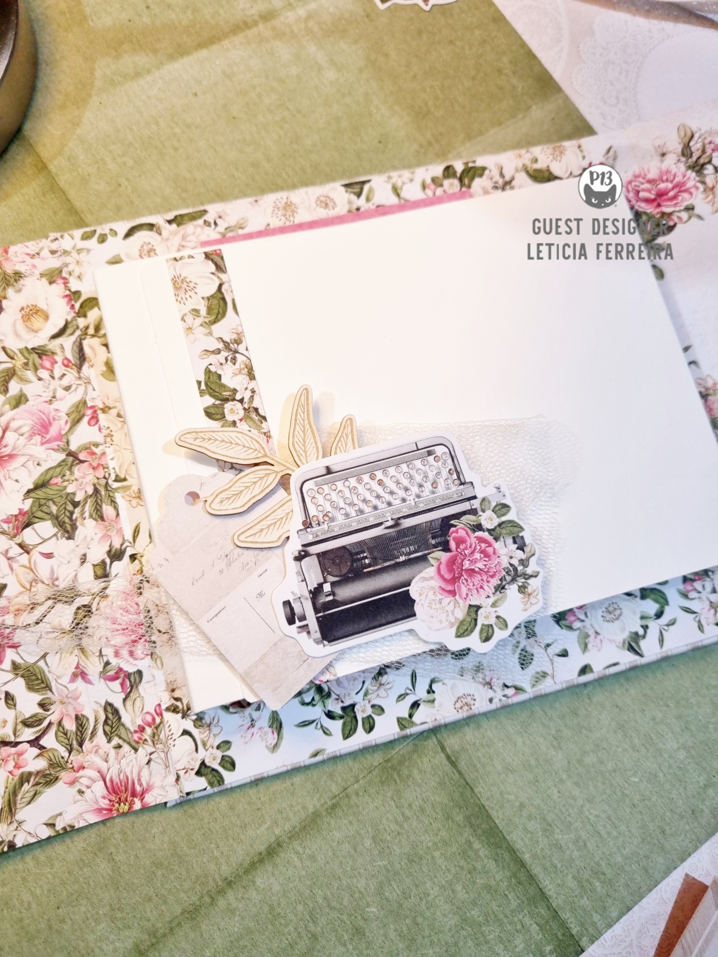 Cartão branco com máquina de escrever e flores sobre fundo floral e tecido verde