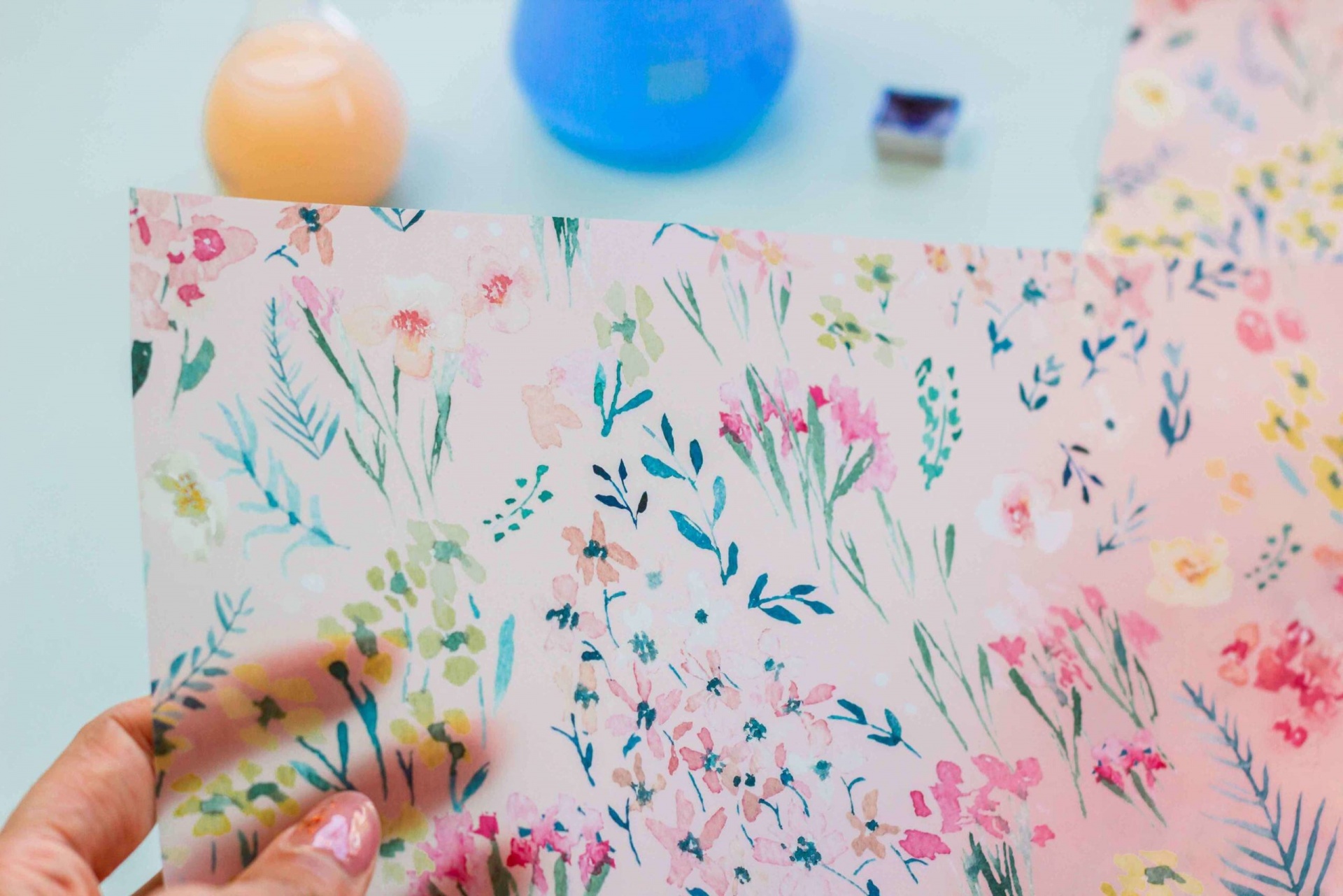 Papel de transferência floral colorido segurado por mão com frascos desfocados ao fundo