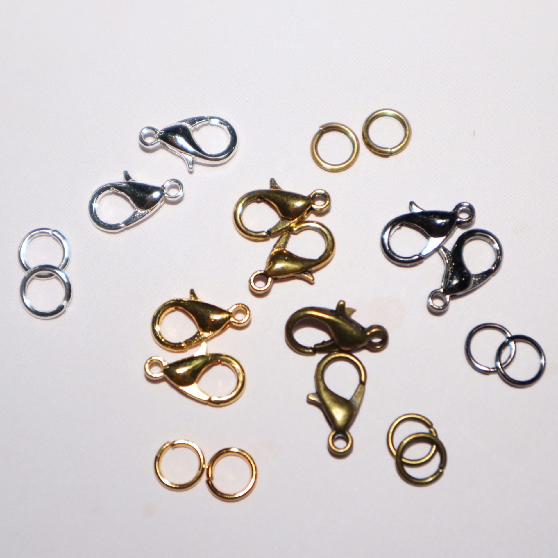 Fechos de lagosta e argolas metálicas em várias cores numa superfície branca