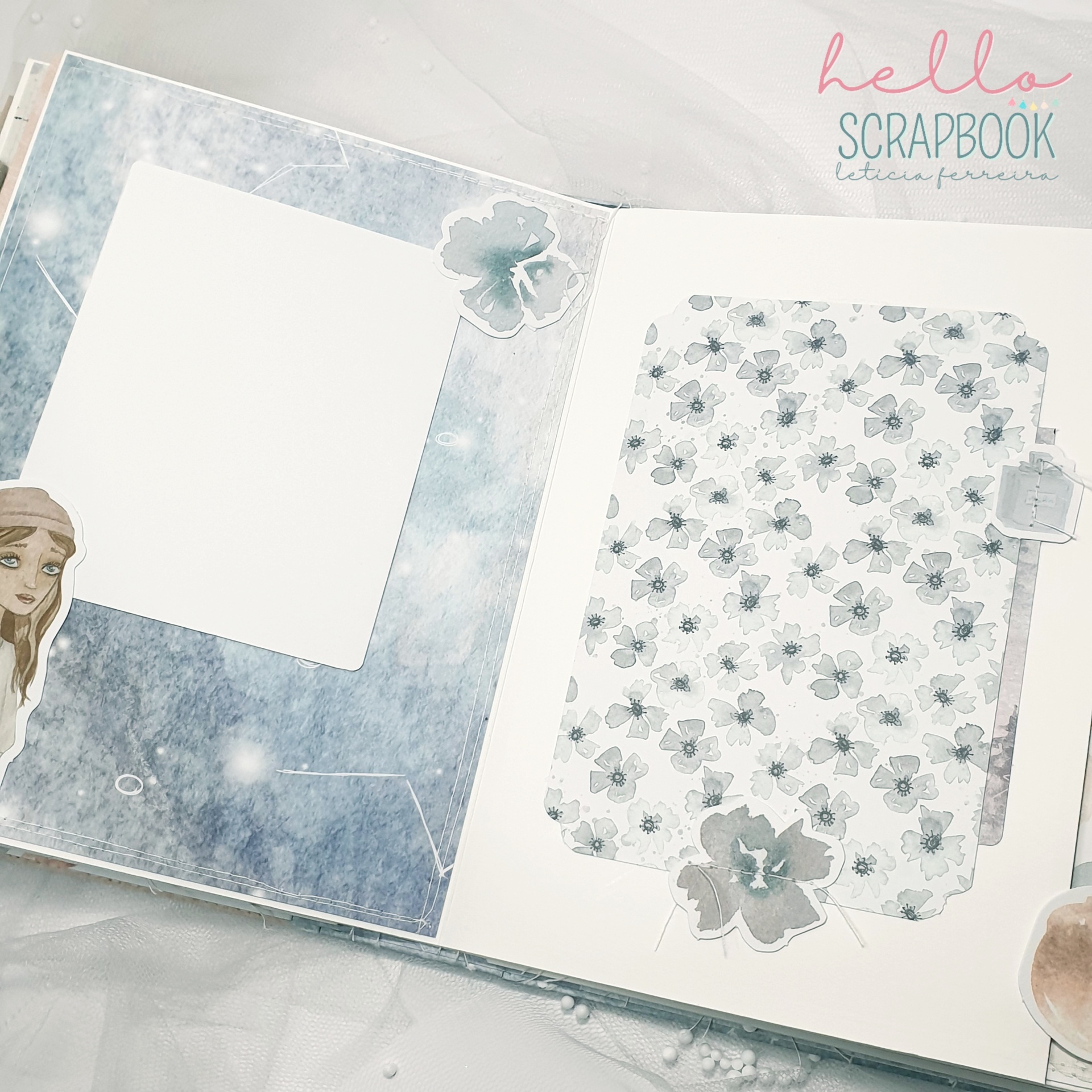 Álbum de scrapbook azul e cinza aberto com decoração floral e espaço para fotos