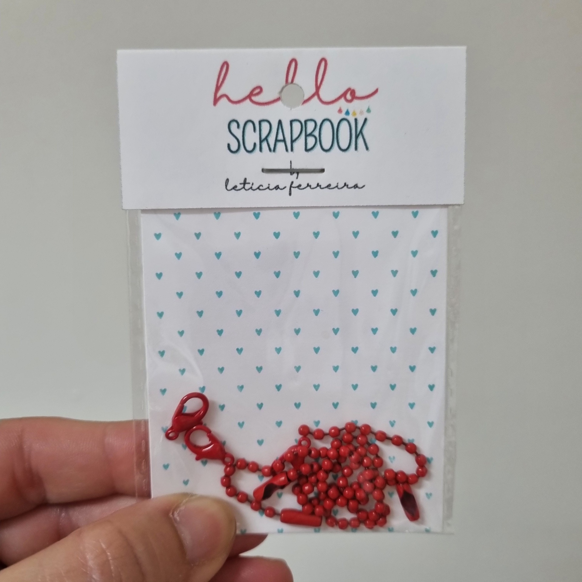 Correntes vermelhas em embalagem transparente com cartão de fundo branco com corações azuis e texto hello SCRAPBOOK by leticia ferreira