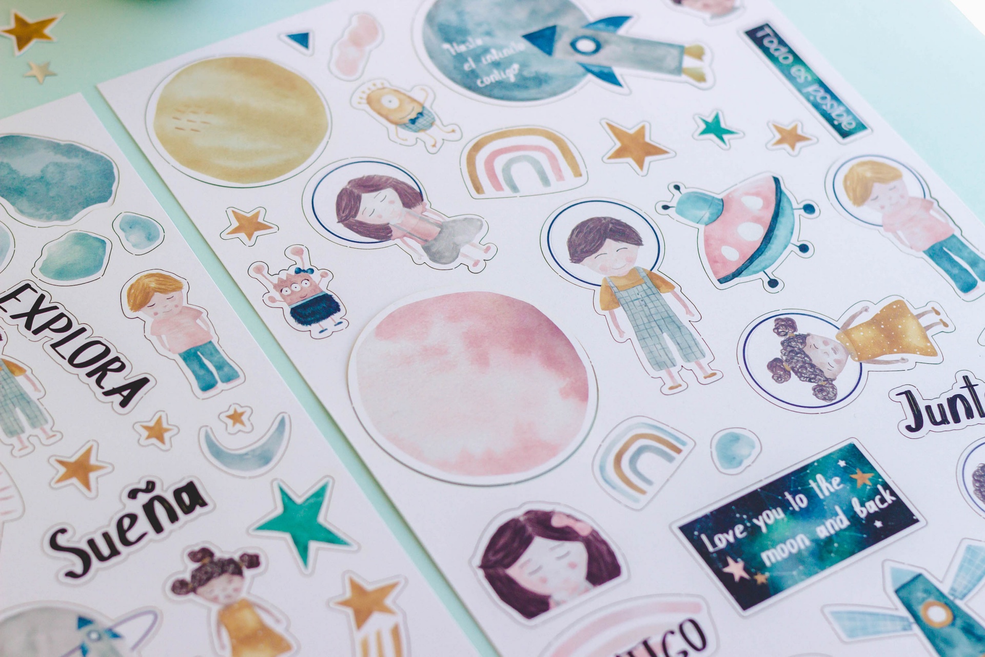 Folhas de autocolantes coloridos com temas espaciais e textos em inglês e espanhol