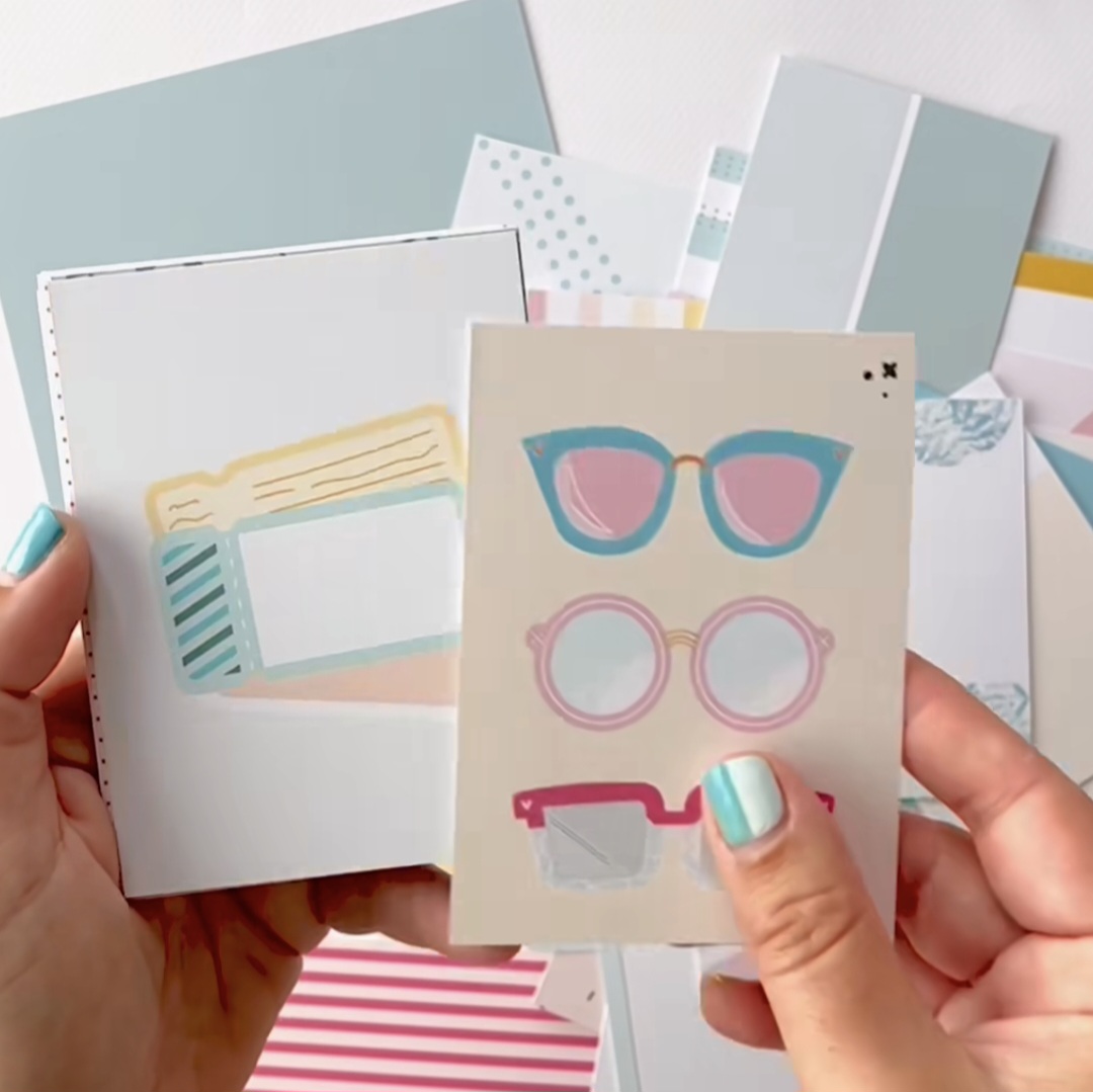 Cartões de papel coloridos com desenhos de óculos e gráficos segurados por mãos com unhas azuis