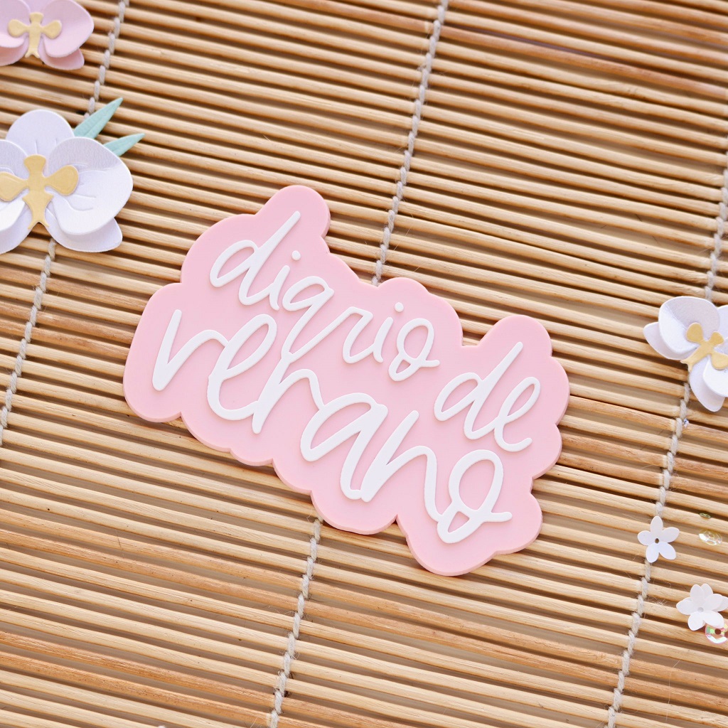 Etiqueta rosa claro com texto 'diário de verão' sobre esteira de madeira clara com flores de papel coloridas