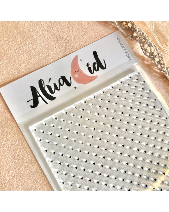 Folha de autocolantes transparentes com brilhos prateados em embalagem com etiqueta 'Alúa Cid' em superfície bege