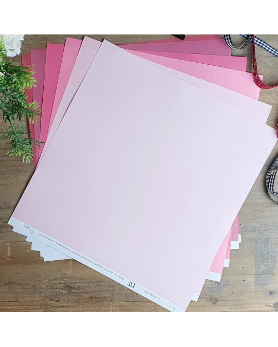 Folhas quadradas de papel rosa em vários tons sobre mesa de madeira com ramos e fitas