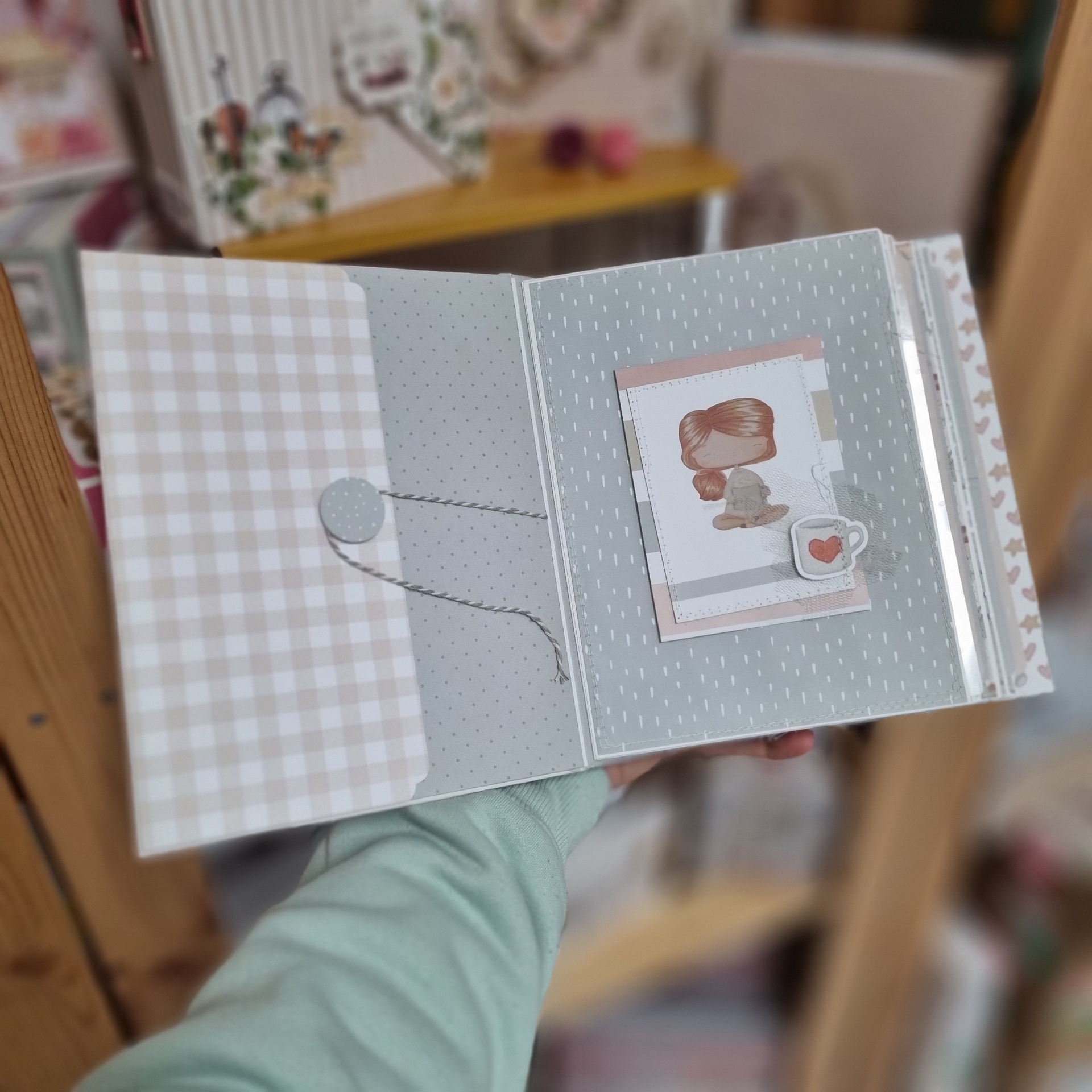 Álbum ou caderno aberto com ilustração de menina e chávena com coração em padrão cinza e bege.