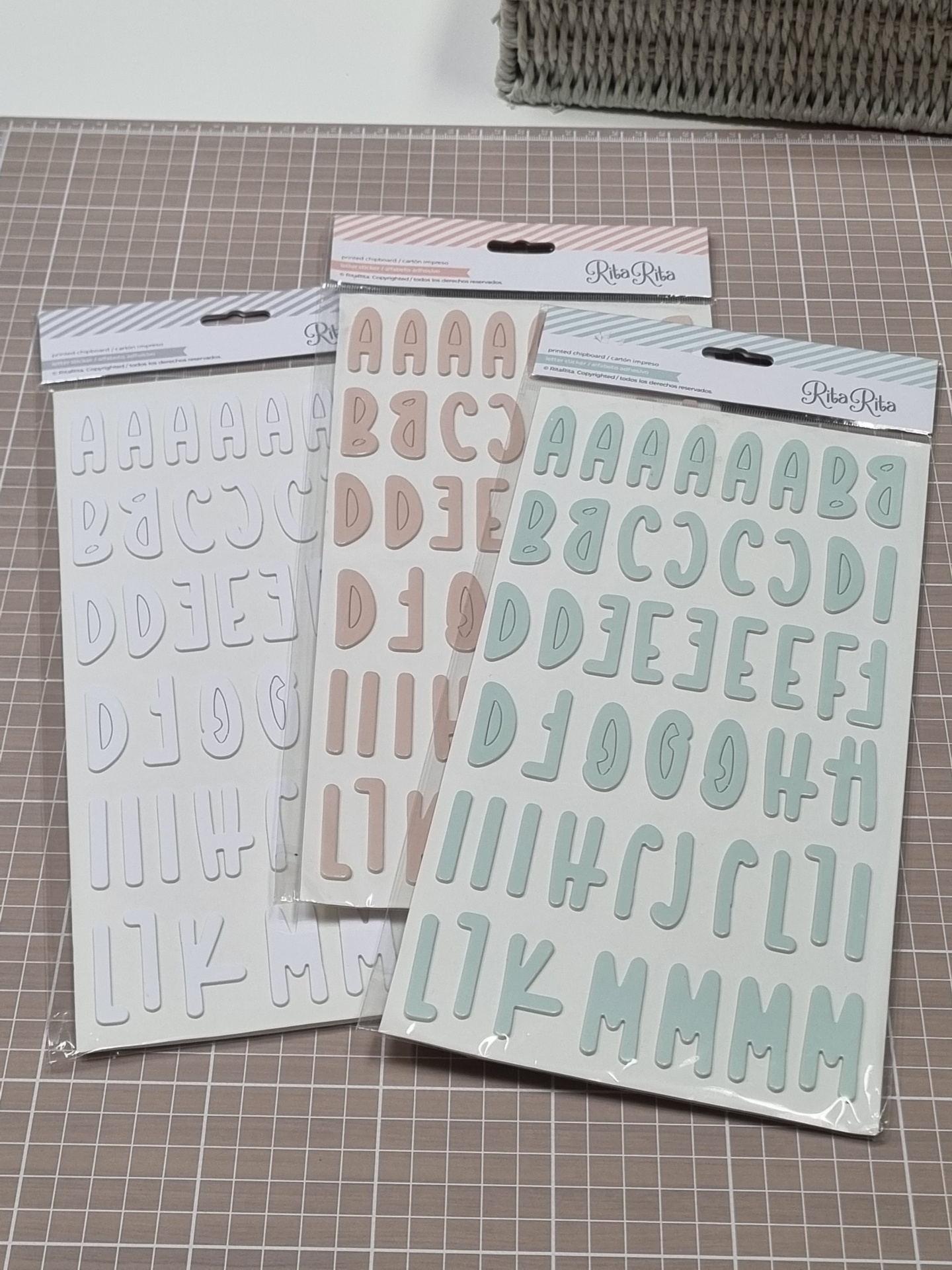 Autocolantes de letras em cartelas coloridas em tons pastel sobre mesa com padrão de grelha e cesta de vime