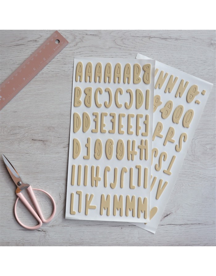 Cartazes com letras adesivas bege, régua rosa e tesoura rosa num fundo de madeira clara