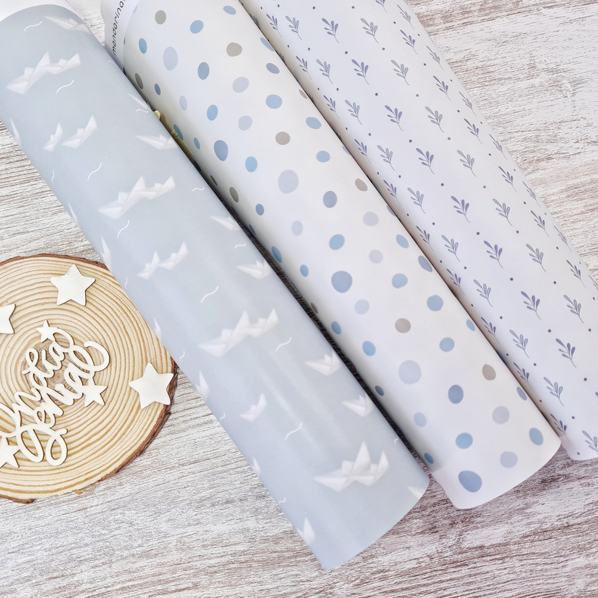 Três rolos de papel decorativo azul claro e branco com diferentes padrões sobre superfície de madeira