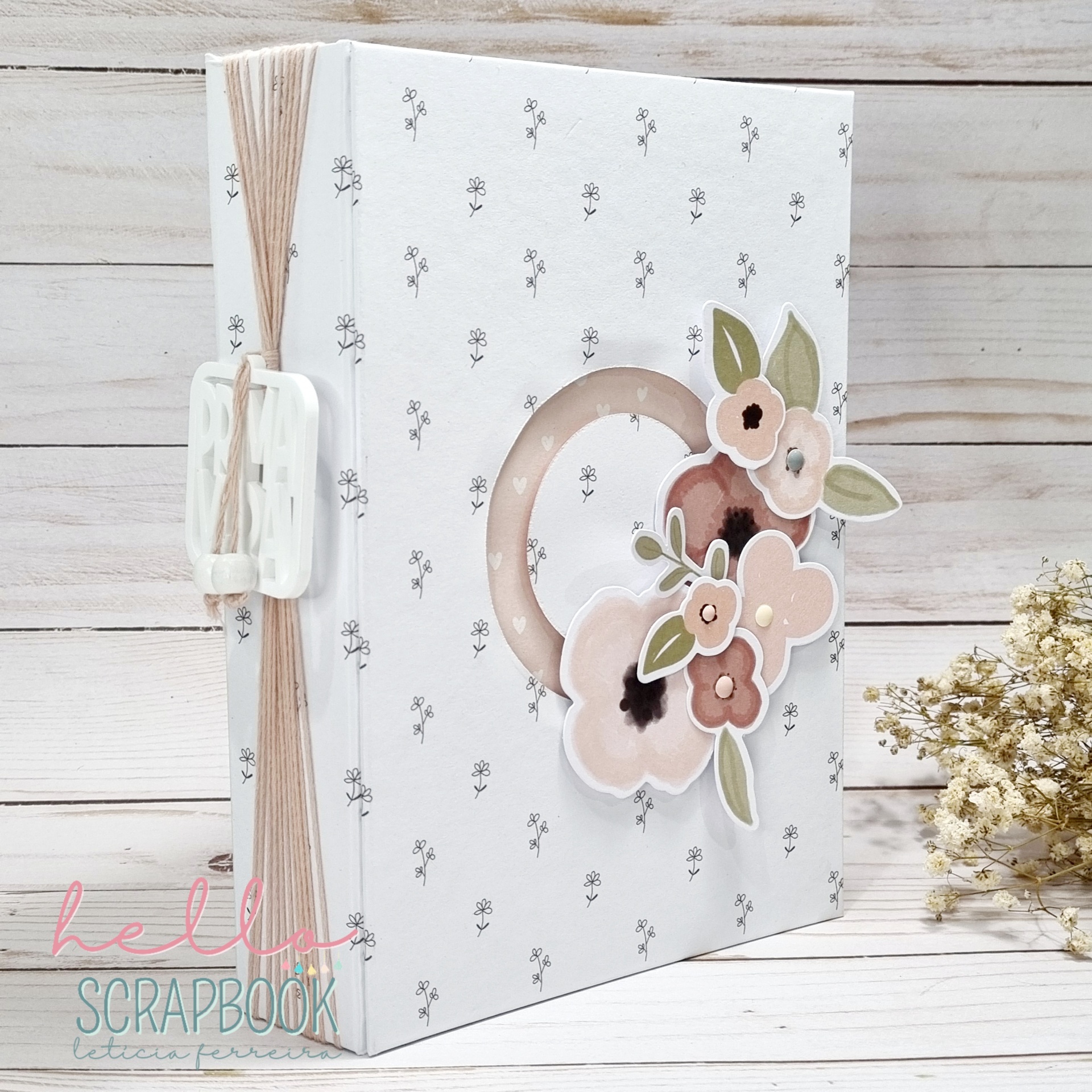 Álbum de scrapbook branco com decoração de flores em tons rosa e castanho e encadernação com argolas plásticas e cordões de sisal