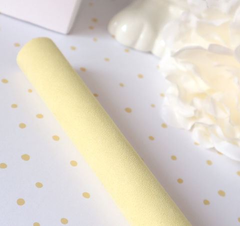Rolo amarelo claro com textura suave sobre papel branco com pontos dourados e tecidos brancos ao fundo