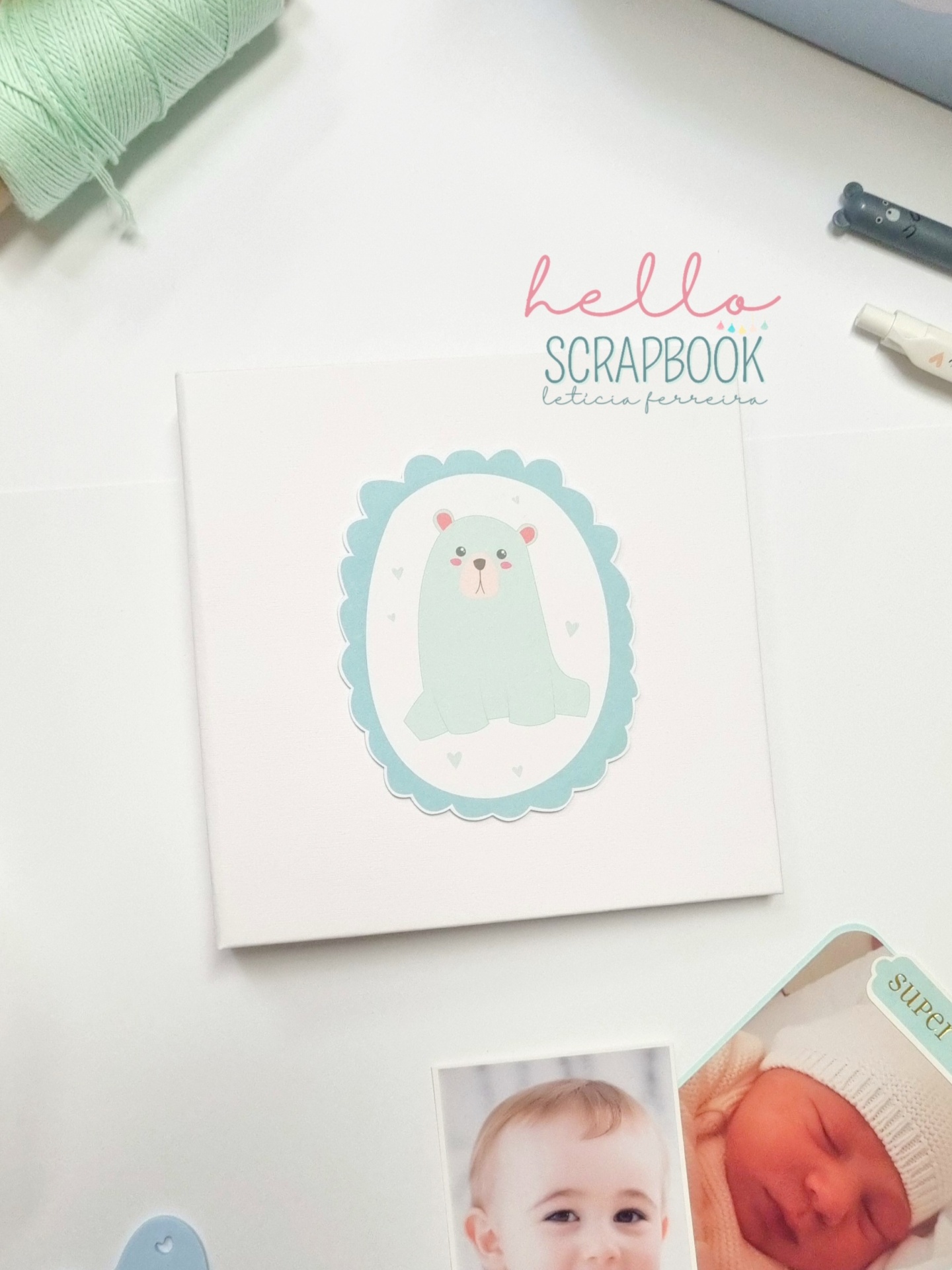 Álbum com ilustração de foca azul claro e borda scalloped azul sobre mesa branca com fotos de bebés.