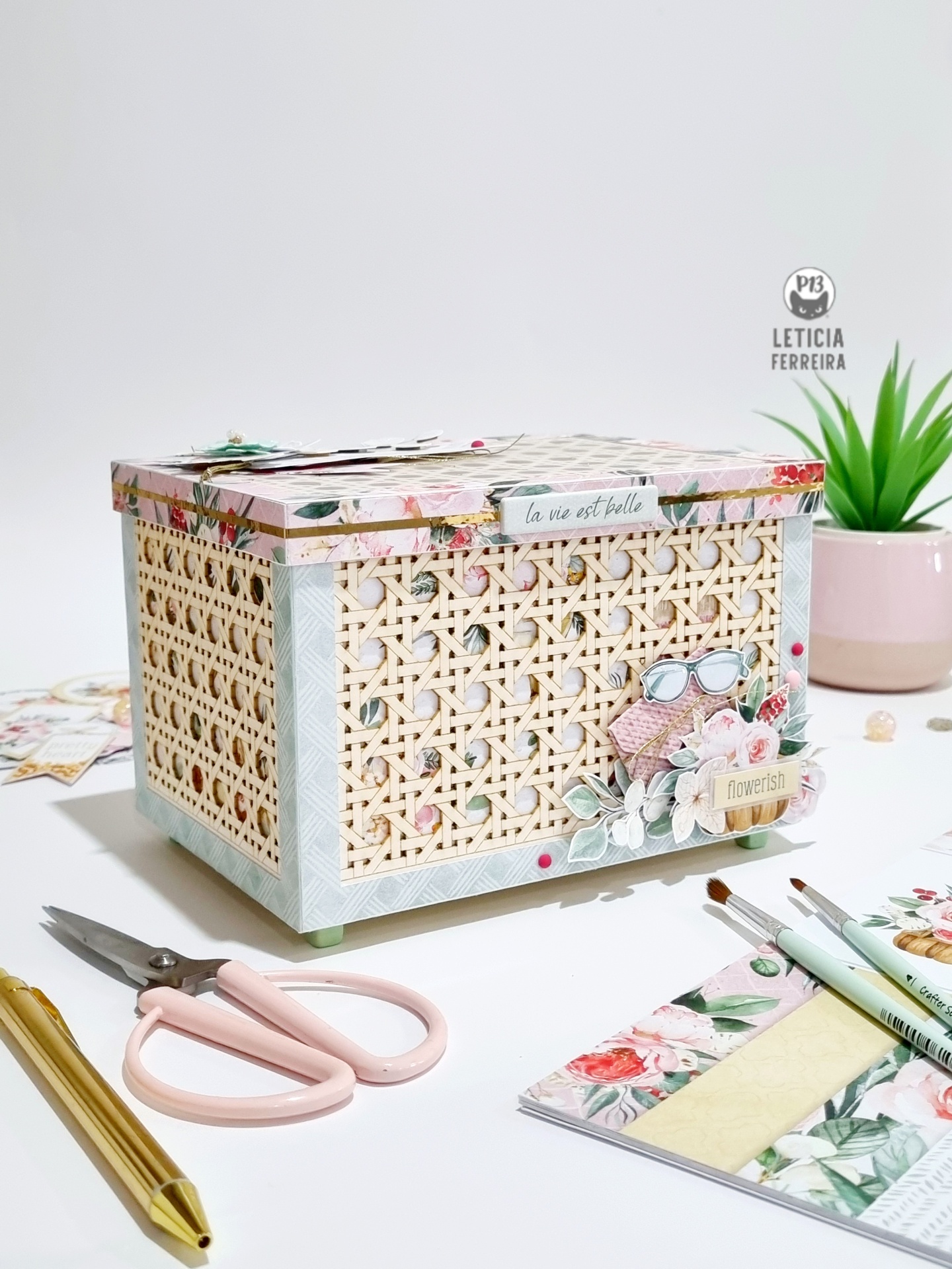 Caixa decorativa em rattan com decoração floral, etiqueta e objetos de escritório