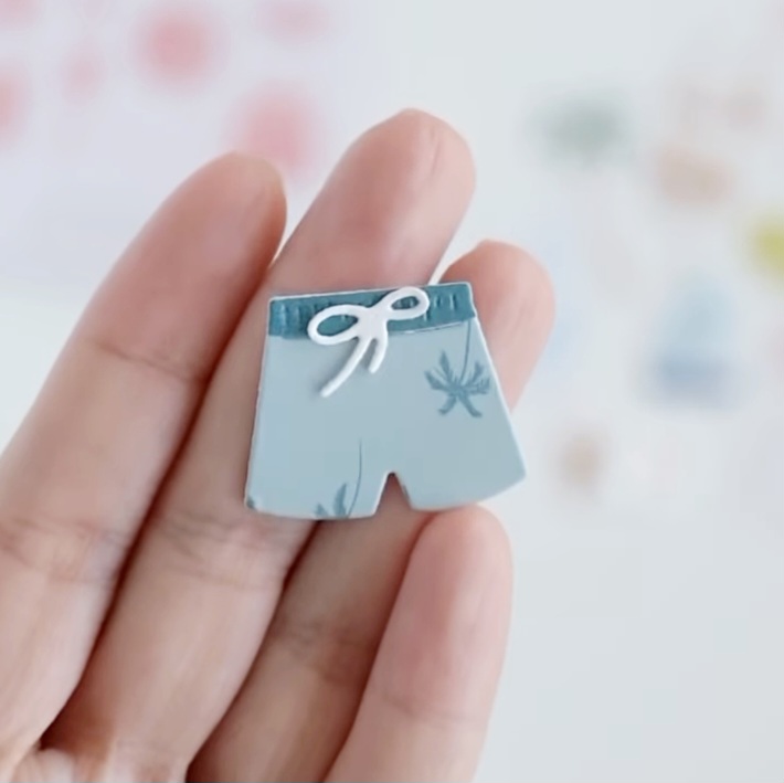 Miniatura ou pin azul claro em forma de calções com cordão branco